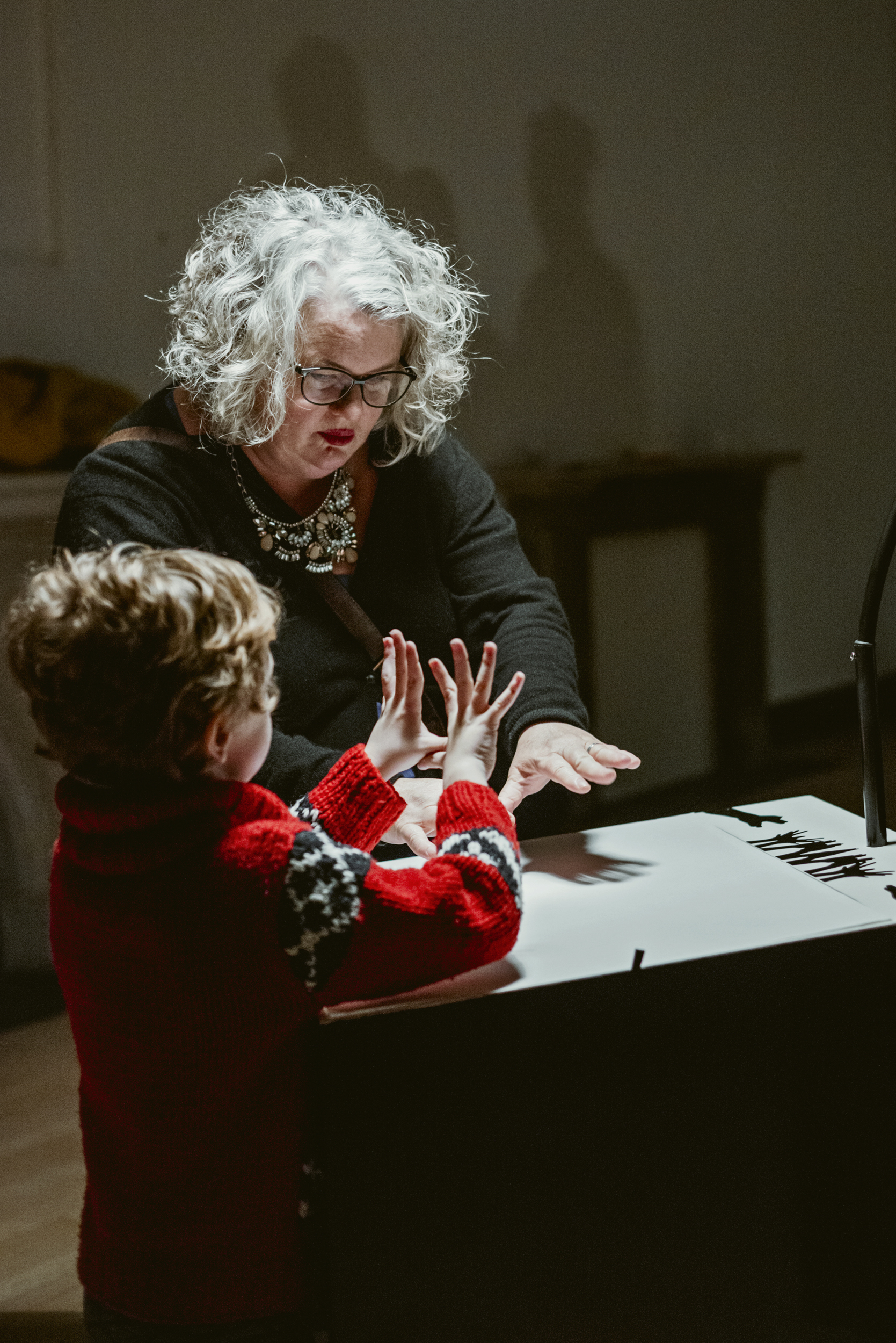 An adult and child hold their hands over an illuminated table to make music with shadows.